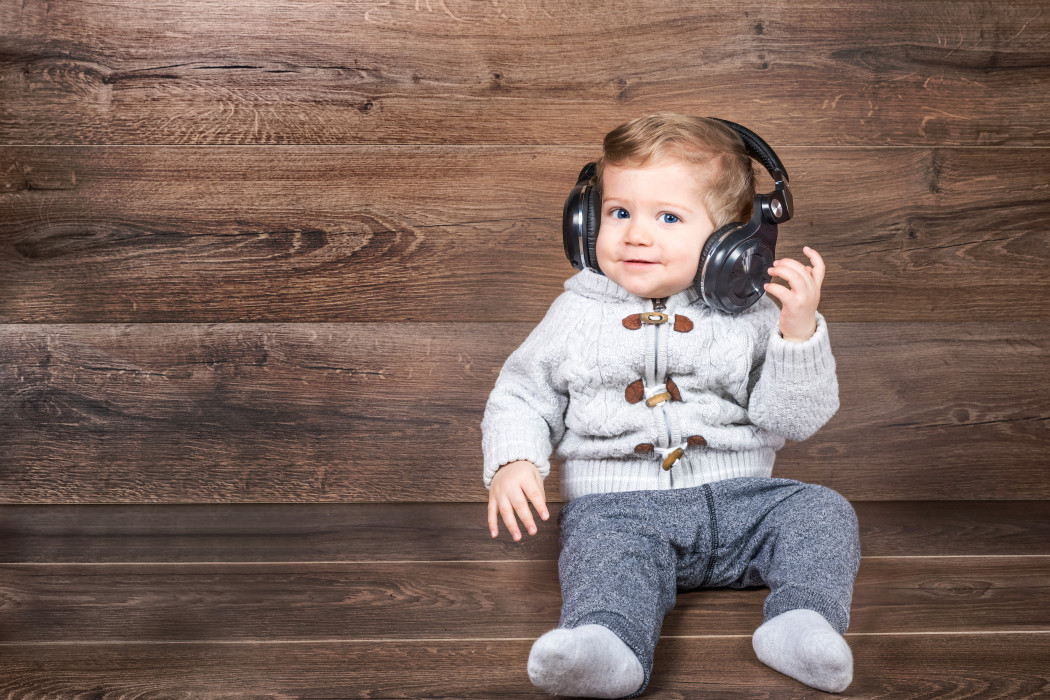 Baby boy smiling on wooden background with bluetooth/wireless headphones.